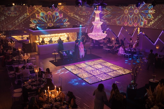 Een feestzaal met verlichte dansvloer en kroonluchter.