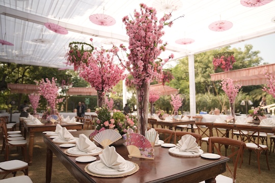 Sfeervol gedekte feesttafel met roze kersenbloesem en hangende parasols.